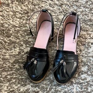 Women’s black shoes with low heel, ankle strap, and tassel feature.